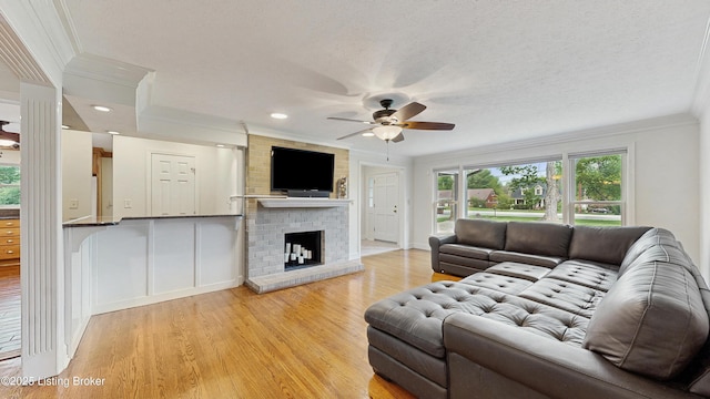 living room with ornamental molding, a ceiling fan, light wood finished floors, and a brick fireplace