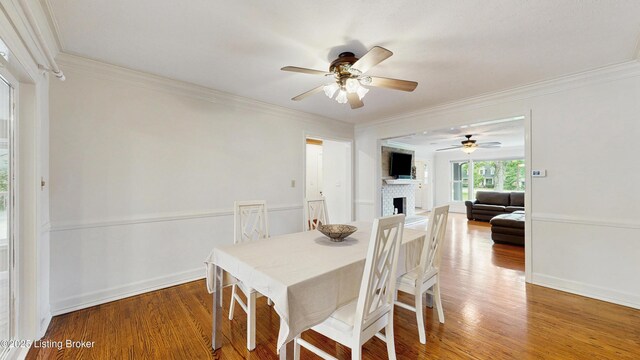 dining area featuring a brick fireplace, a ceiling fan, crown molding, and wood finished floors