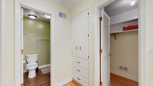 bathroom featuring toilet, visible vents, wood finished floors, and a closet