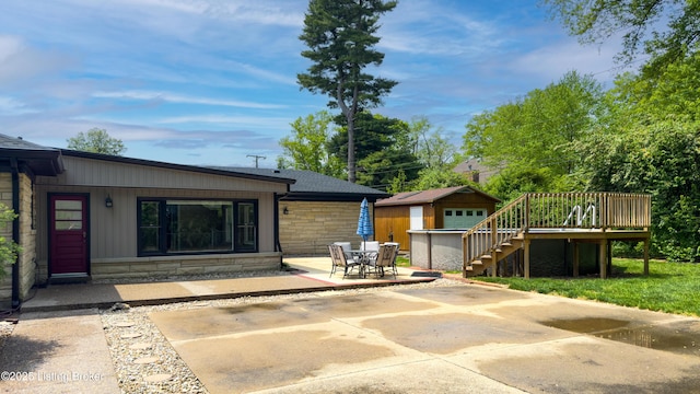 rear view of house with an outdoor structure, stone siding, a deck, stairs, and a patio area