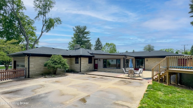 rear view of house featuring a patio, an attached garage, stone siding, and a deck