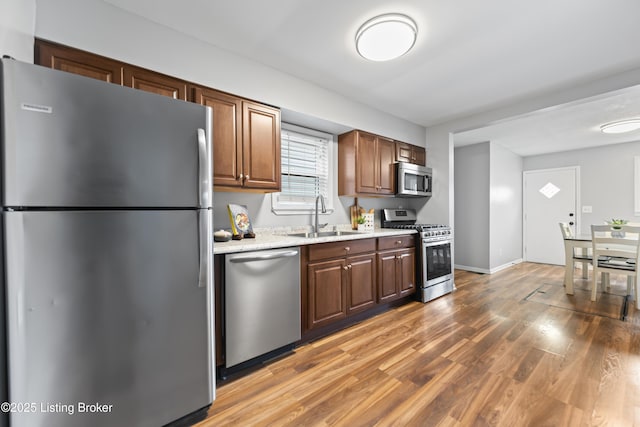 kitchen with baseboards, appliances with stainless steel finishes, a sink, and light wood-type flooring