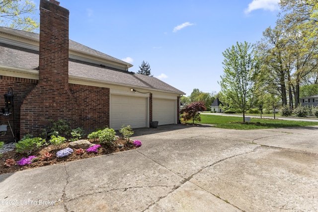 view of home's exterior featuring concrete driveway, brick siding, a chimney, and a garage