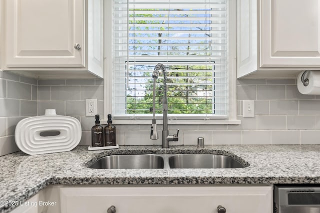 kitchen featuring decorative backsplash, stainless steel dishwasher, a sink, light stone counters, and white cabinets
