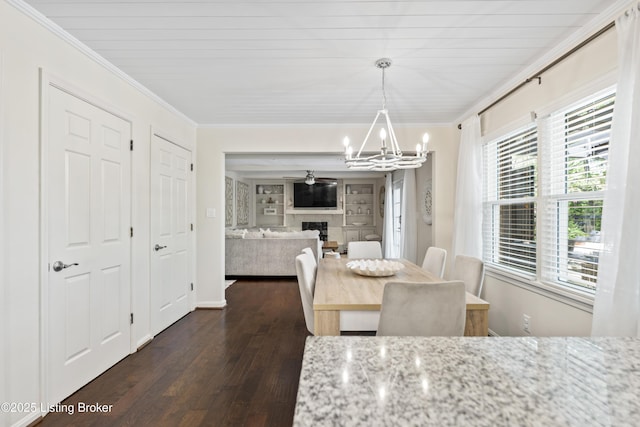 dining space with crown molding, a fireplace, dark wood finished floors, and a notable chandelier