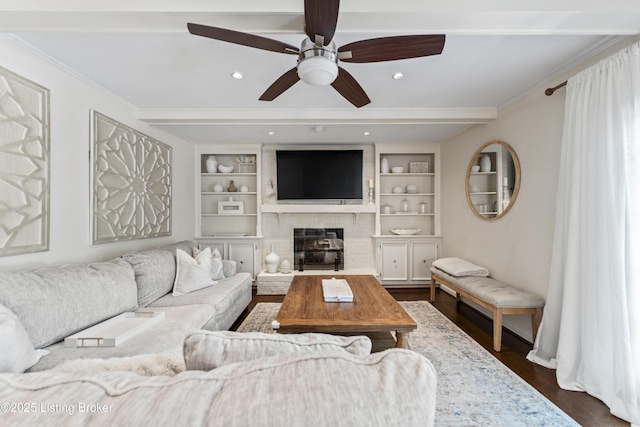living room with ornamental molding, beamed ceiling, dark wood-style floors, built in shelves, and a ceiling fan
