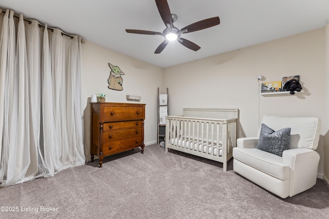 carpeted bedroom featuring a nursery area and a ceiling fan