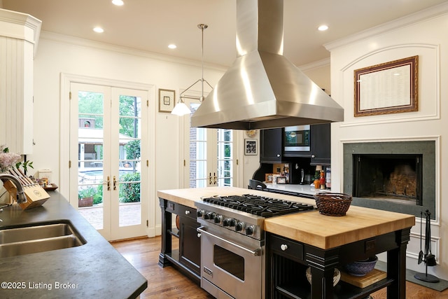 kitchen with butcher block counters, island exhaust hood, french doors, dark cabinetry, and high end stove