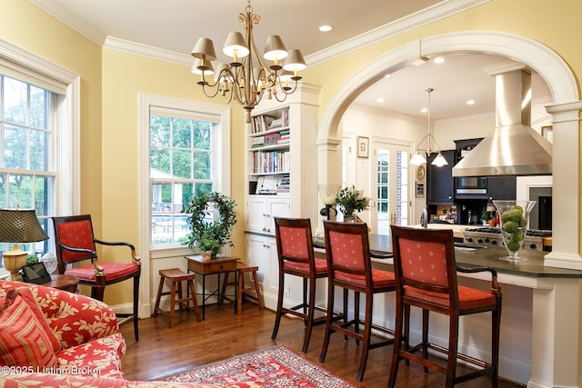 dining area featuring arched walkways, a chandelier, plenty of natural light, and wood finished floors