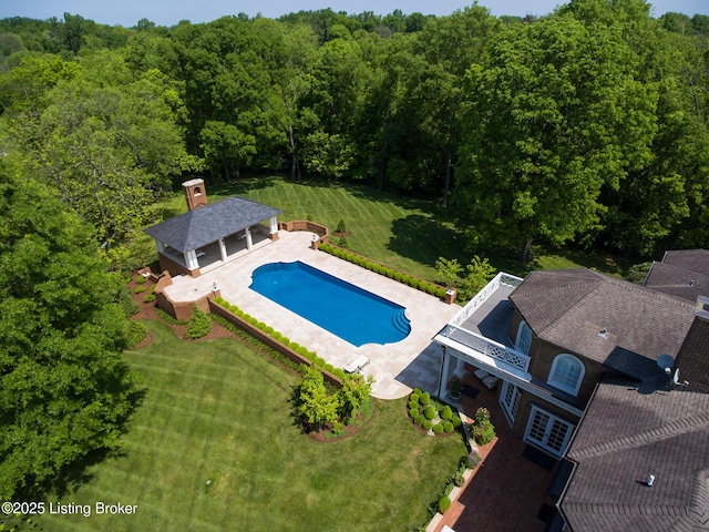 outdoor pool featuring a lawn, an outbuilding, a patio, and a forest view