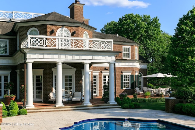 back of property featuring an outdoor pool, a patio area, brick siding, and a balcony