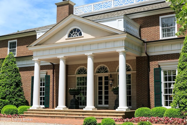 property entrance with covered porch, brick siding, and a chimney