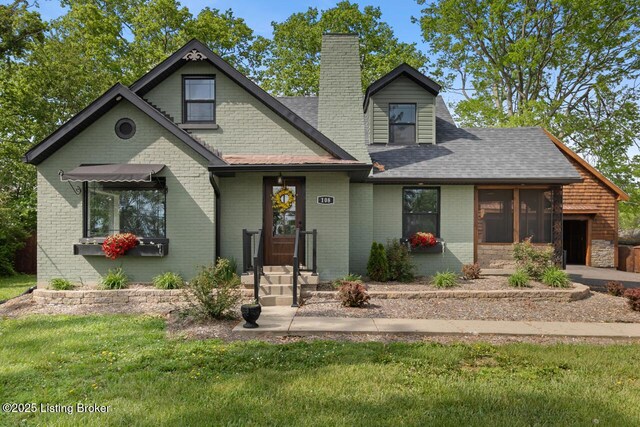 view of front of house with brick siding, a shingled roof, a front yard, and a chimney