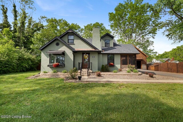 view of front of home featuring a chimney, brick siding, fence, a front lawn, and an attached garage