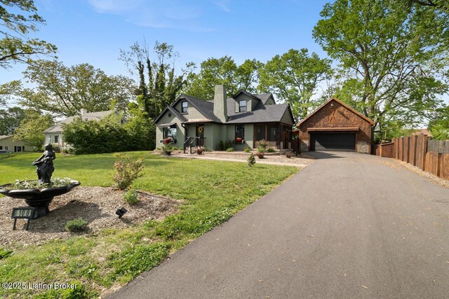 view of front of home with fence, a chimney, a front yard, and aphalt driveway