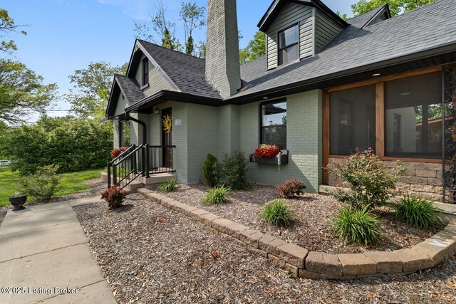 view of property exterior with brick siding, roof with shingles, a sunroom, and a chimney