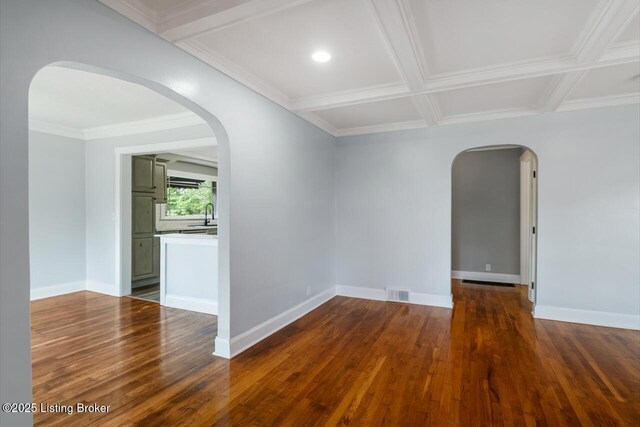 empty room featuring arched walkways, baseboards, visible vents, and dark wood-style floors
