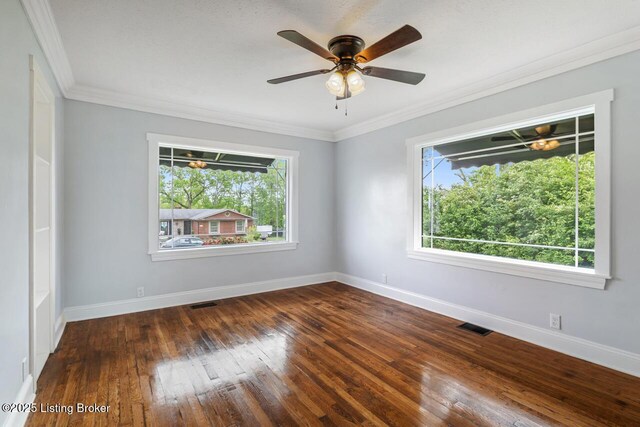 empty room with wood-type flooring, ornamental molding, baseboards, and visible vents