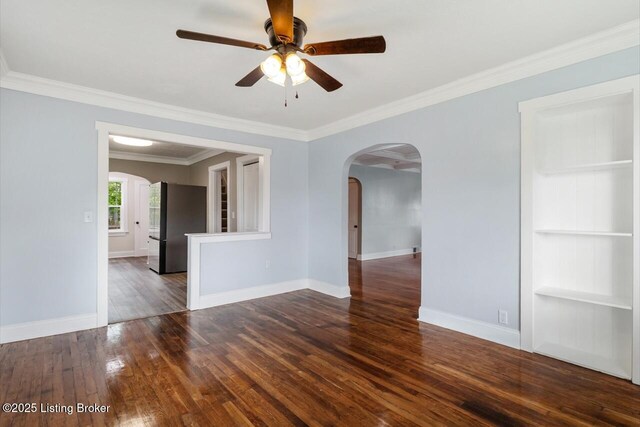 spare room featuring wood-type flooring, arched walkways, baseboards, and ceiling fan