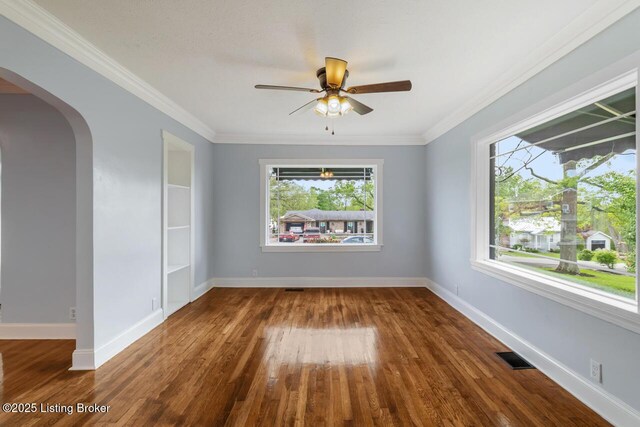 spare room featuring ceiling fan, visible vents, arched walkways, wood finished floors, and ornamental molding