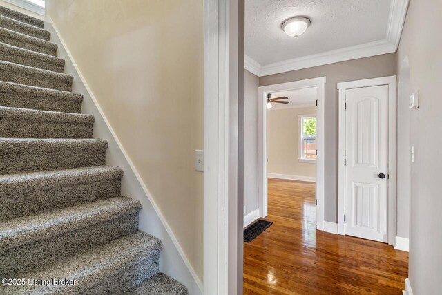 staircase with a textured ceiling, baseboards, wood finished floors, visible vents, and ornamental molding