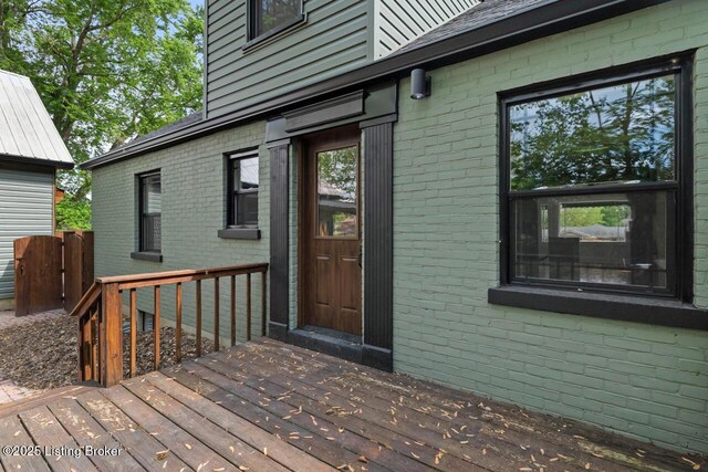 view of exterior entry with brick siding and a wooden deck