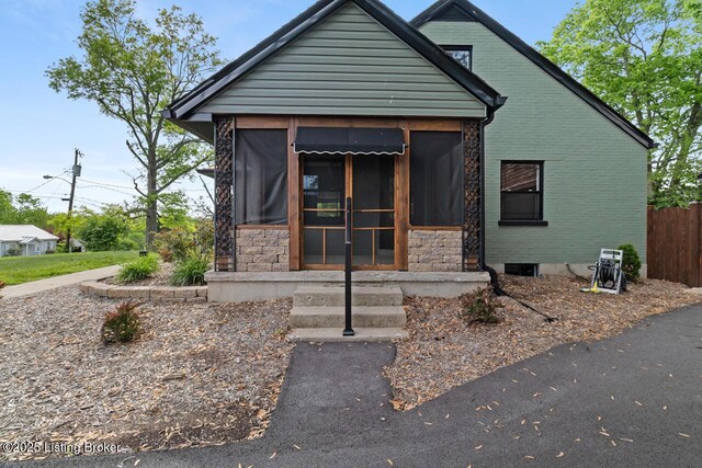 view of front of house with a sunroom, fence, and stone siding
