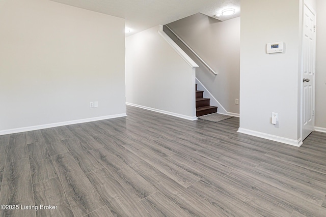 unfurnished living room featuring stairs, baseboards, and wood finished floors