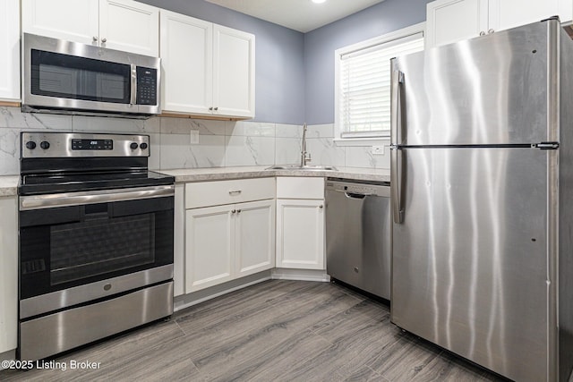 kitchen with decorative backsplash, appliances with stainless steel finishes, wood finished floors, a sink, and white cabinets