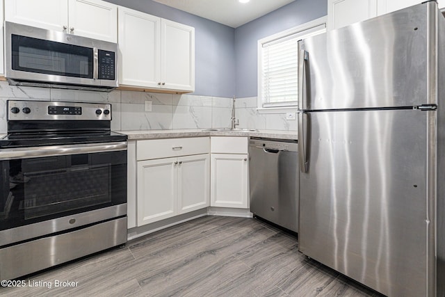 kitchen with decorative backsplash, a sink, light wood finished floors, stainless steel appliances, and white cabinetry