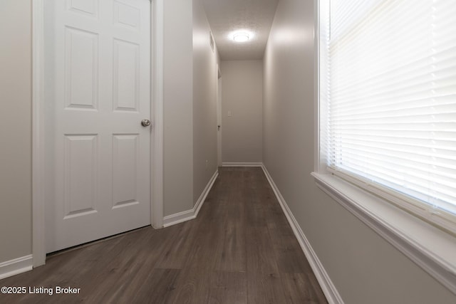 hall with dark wood-style flooring, baseboards, and a textured ceiling