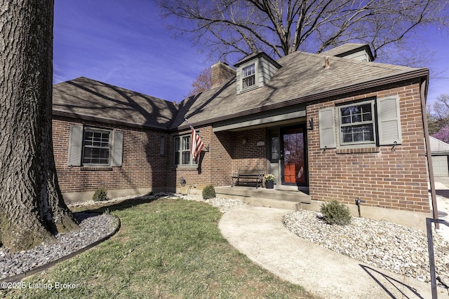 view of front of house featuring brick siding, a chimney, roof with shingles, and a front lawn