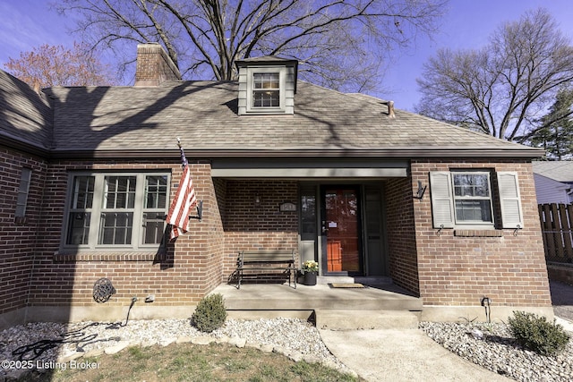 view of exterior entry with brick siding, a chimney, and roof with shingles