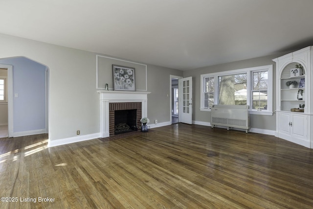 unfurnished living room with baseboards, a fireplace, arched walkways, and wood finished floors