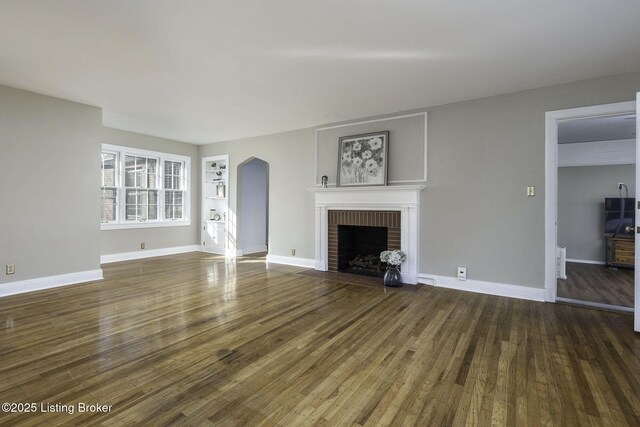 unfurnished living room with baseboards, arched walkways, wood finished floors, and a fireplace