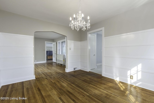 unfurnished dining area featuring arched walkways, baseboards, an inviting chandelier, heating unit, and dark wood-type flooring