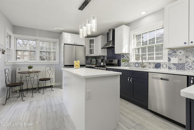 kitchen with a center island, light countertops, wall chimney exhaust hood, a sink, and stainless steel appliances