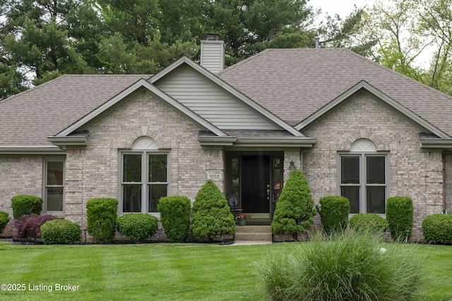 view of front facade with brick siding, a shingled roof, a front lawn, and a chimney