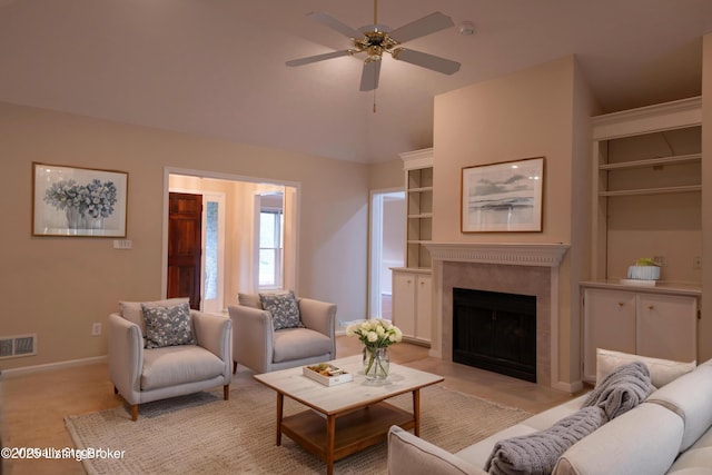 living area with a tiled fireplace, a ceiling fan, baseboards, lofted ceiling, and visible vents