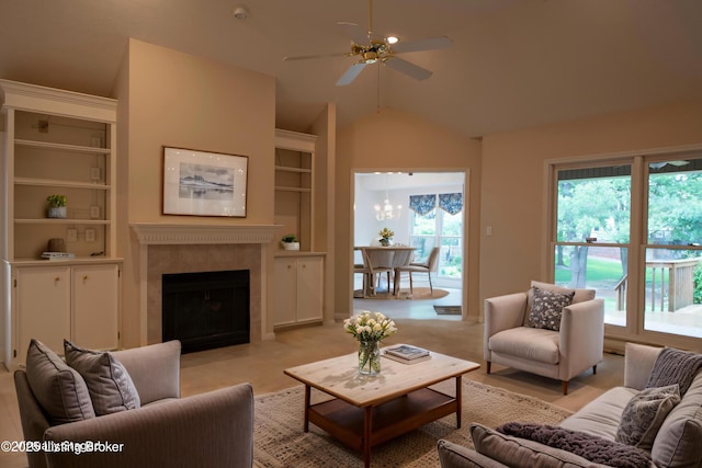living area featuring a premium fireplace, vaulted ceiling, built in shelves, and ceiling fan with notable chandelier