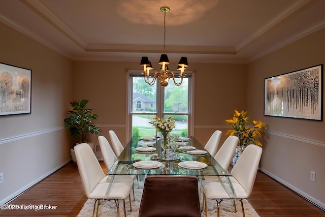 dining room with an inviting chandelier, a raised ceiling, baseboards, wood finished floors, and ornamental molding