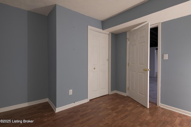 unfurnished bedroom with a closet, baseboards, and dark wood-type flooring