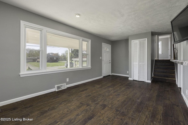 unfurnished living room featuring a textured ceiling, baseboards, dark wood-type flooring, visible vents, and stairway