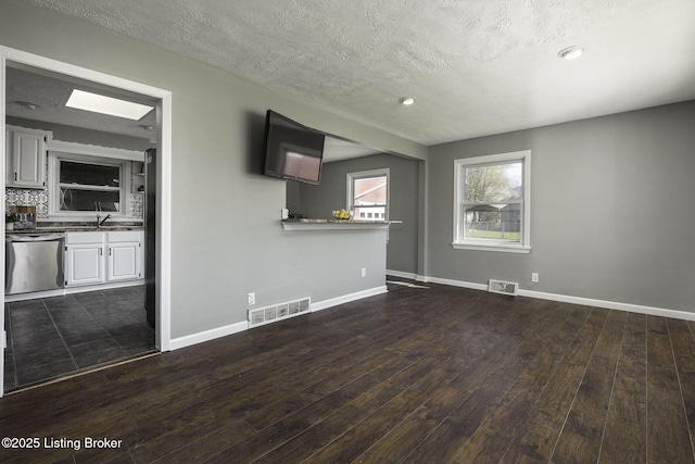 unfurnished living room featuring visible vents, a textured ceiling, baseboards, and dark wood-style floors