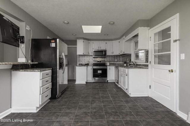 kitchen with white cabinets, a sink, stainless steel appliances, backsplash, and a skylight