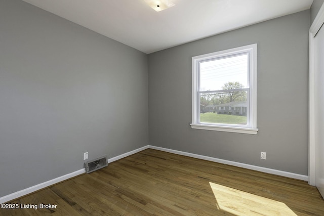 unfurnished room with baseboards, wood finished floors, and visible vents