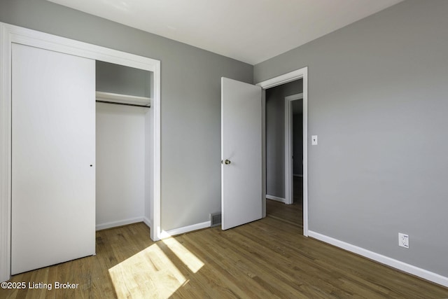 unfurnished bedroom featuring a closet, baseboards, wood finished floors, and visible vents