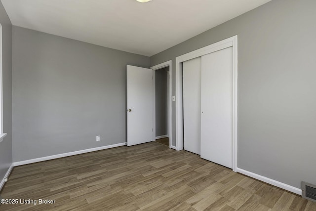 unfurnished bedroom featuring baseboards, a closet, wood finished floors, and visible vents