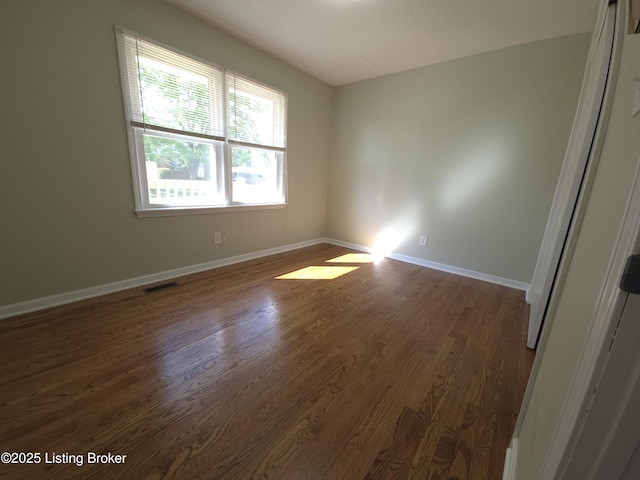 spare room featuring visible vents, baseboards, and dark wood-type flooring