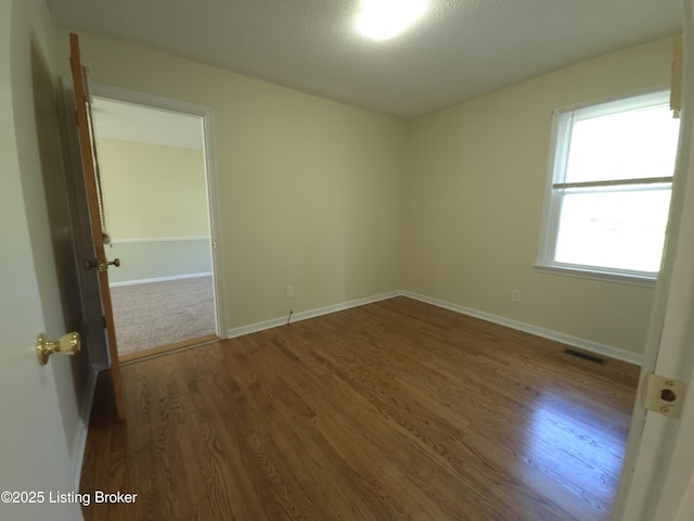 spare room with baseboards, wood finished floors, and visible vents